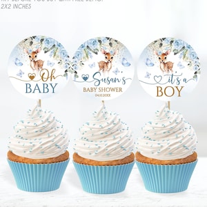 May include: Three blue and white cupcake toppers with a deer and floral design. The toppers say "Oh Baby", "Susan's Baby Shower 04.10.2000", and "It's a Boy".