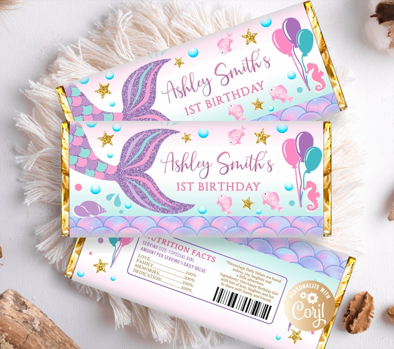 May include: Two pink and blue mermaid-themed chocolate bar wrappers with gold foil accents. The wrappers feature a mermaid tail, seashells, and stars. The text on the wrappers reads "Ashley Smith's 1st Birthday".