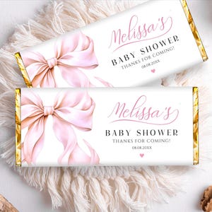 May include: Two white chocolate bar wrappers with a pink bow design. The text "Melissa's Baby Shower Thanks for Coming! 08.08.20XX" is printed on each wrapper.