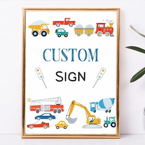 May include: A framed print featuring colorful illustrations of various vehicles, including a dump truck, fire truck, and train. The words "CUSTOM SIGN" are displayed in blue and black font. The print is in a gold frame.