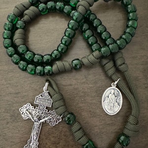 May include: A green paracord rosary with green glass beads, a silver crucifix with the inscription "JESUS NAZARENO REY DE REYES", and a silver medal of Saint Patrick.