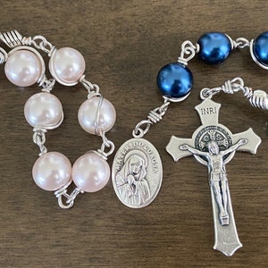 Peut inclure: Deux chapelets avec des crucifix et des médaillons en argent. Un chapelet a des perles roses et l'autre a des perles bleu foncé.