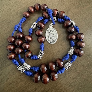 May include: A brown wooden rosary with blue cord and silver accents. The centerpiece features a silver medal of Saint Michael the Archangel.