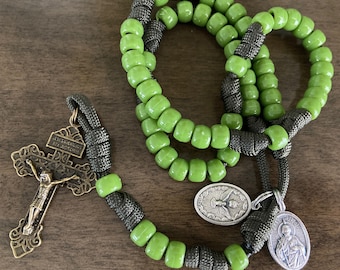 May include: Green and black rosary beads with a silver crucifix and two silver medallions. The crucifix features a figure of Jesus Christ and the medallions feature religious imagery.