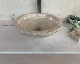 May include: A white stone vessel sink with a rough, textured exterior. The sink is oval-shaped and has a smooth, white interior.