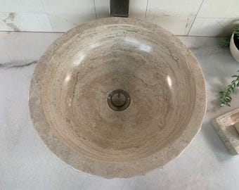 May include: A round, beige stone vessel sink with a smooth, textured surface. The sink has a single drain hole in the center.
