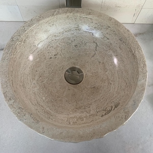 May include: A round, white stone bathroom sink with a silver drain.