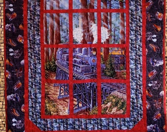 May include: A red, blue, and white quilt with a framed image of a train traveling through a forest. The train is blue and has white smoke coming from the chimney. The forest is green and brown. The frame is red and has a blue and white border.