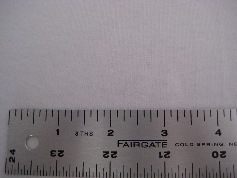 May include: A close-up of a silver metal ruler with black markings. The ruler is labeled "FAIRGATE" and "COLD SPRING, NE". The ruler is marked in inches and 8ths of an inch.