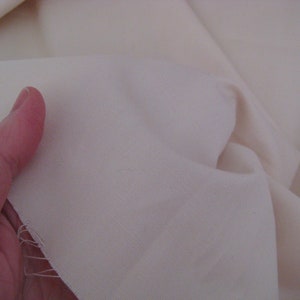 May include: Close-up of a smooth, off-white fabric. The fabric is folded and has a slight sheen.