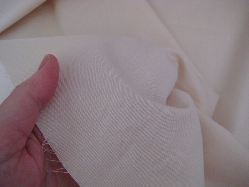 May include: Close-up of a smooth, off-white fabric. The fabric is folded and has a slight sheen.