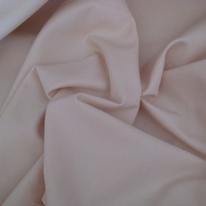 May include: A close-up of a smooth, pale peach-colored fabric. The fabric is folded and draped, showing its soft texture.