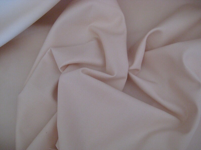 May include: A close-up of a smooth, pale peach-colored fabric. The fabric is folded and draped, showing its soft texture.