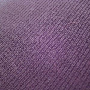 May include: Close-up of a purple fabric with a textured, woven pattern.