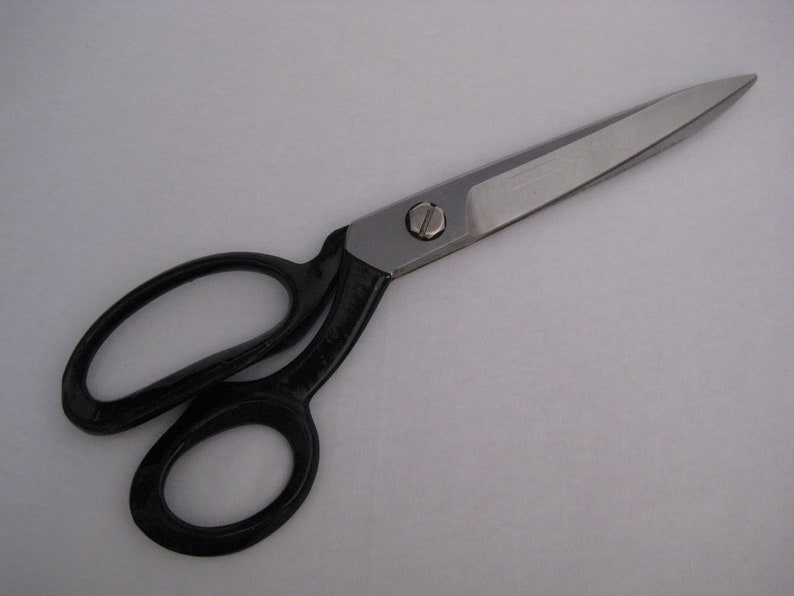 May include: A pair of black handled scissors with a silver blade. The scissors are open and the blade is pointed.