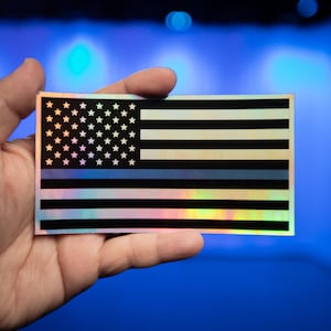 May include: A holographic sticker of the American flag with a thin blue line across the middle.