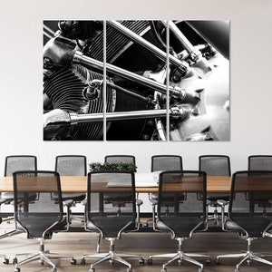 Könnte beinhalten: Schwarz-Weiß-Triptychon-Leinwanddruck eines Vintage-Flugzeugmotors. Die Nahaufnahme zeigt die Zylinder, Rohre und Metallkomponenten des Motors. Das Kunstwerk wird über einem Konferenztisch mit schwarzen Stühlen ausgestellt.