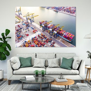 May include: An aerial view of a busy shipping port with a large cargo ship docked at the pier. The ship is loaded with colourful shipping containers. Several cranes are visible in the background, loading and unloading containers.