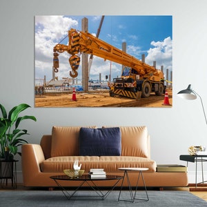 May include: A yellow construction crane with a hook is parked on a construction site. The crane is on a dirt road with a blue sky and white clouds in the background.