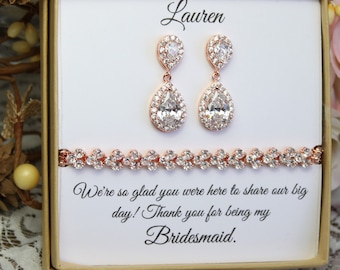 May include: A white gift box with a gold trim and a message inside that reads "We're so glad you were here to share our big day! Thank you for being my Bridesmaid." The box contains a rose gold bracelet and earrings with clear stones.