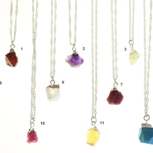 May include: Twelve silver necklaces with different colored gemstone pendants. The pendants are all rough-cut and have a natural, raw look. The necklaces are all the same length and have a delicate chain.
