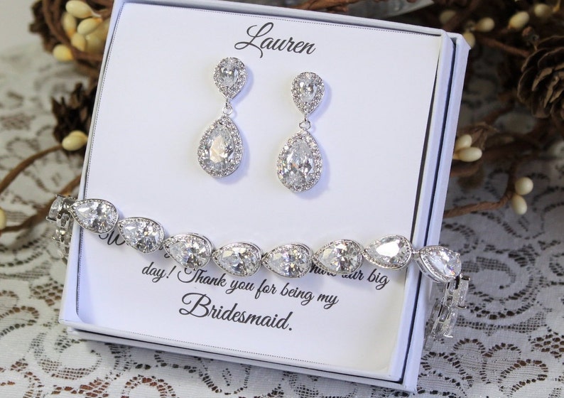 May include: A white gift box with a silver bracelet and earrings. The box has the name "Lauren" written on it and the message "Thank you for being my bridesmaid."