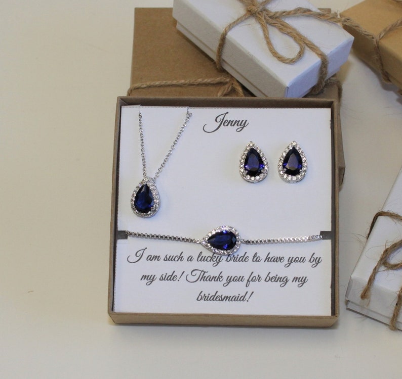 May include: A gift box with a blue teardrop necklace, earrings, and bracelet set. The box has a card inside that says "Jenny I am such a lucky bride to have you by my side! Thank you for being my bridesmaid!"
