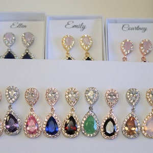 May include: Eight pairs of dangle earrings with pear-shaped stones in various colors, including green, blue, purple, pink, and yellow. Each earring has a clear crystal halo around the stone.
