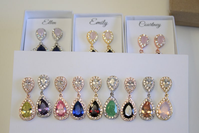 May include: Eight pairs of dangle earrings with pear-shaped stones in various colors, including green, blue, purple, pink, and yellow. Each earring has a clear crystal halo around the stone.