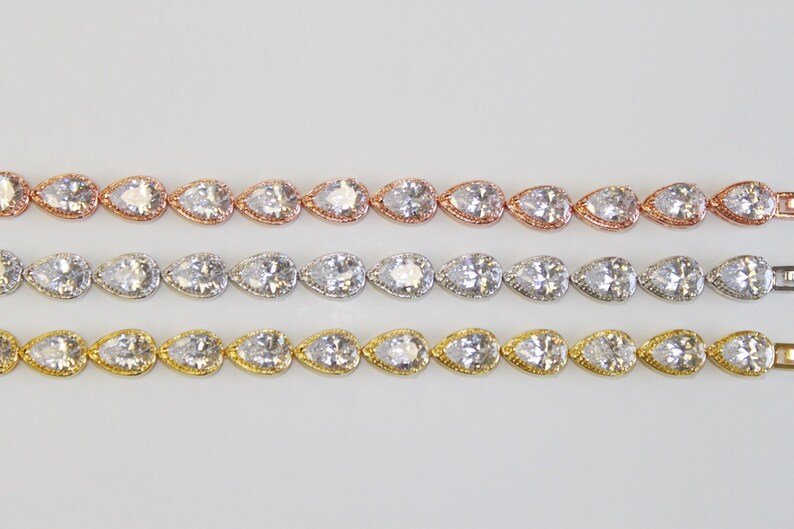 May include: Three rows of pear-shaped crystal bracelets in rose gold, silver, and gold settings.