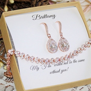 May include: A rose gold jewelry set with a delicate bracelet and teardrop earrings. The set comes in a box with a personalized message that reads "My "I do" would not be the same without you!"