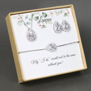 May include: A gift box with a personalized message for a bridesmaid. The box contains a silver necklace, earrings, and bracelet with teardrop-shaped crystals.