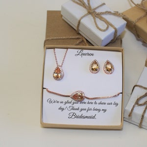 May include: A gift box with a rose gold necklace, earrings, and bracelet with a pear-shaped stone. The box has a personalized message that says "Lauren We're so glad you were here to share our big day! Thank you for being my Bridesmaid."