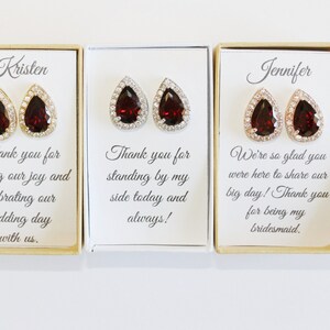 May include: Three small gift boxes with red teardrop earrings inside. The boxes have personalized messages for the recipients, Kristen, Jennifer, and another person whose name is not visible. The messages express gratitude for their support and participation in a wedding.