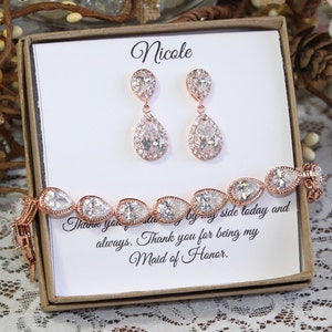 May include: A gift box with a white card that says "Nicole" and "Thank you for being my Maid of Honor." The box contains a rose gold bracelet and earrings with pear-shaped clear stones.