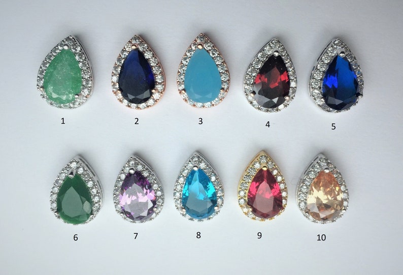May include: Ten teardrop-shaped pendants with different colored gemstones surrounded by a halo of clear cubic zirconia stones. The pendants are numbered 1 through 10.