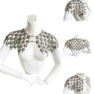 May include: Silver chainmail shoulder piece with a decorative design. The chainmail is made of small, round links that are connected together to form a mesh-like fabric. The shoulder piece is designed to be worn over the shoulders and chest, and it has a flowing, draping effect.