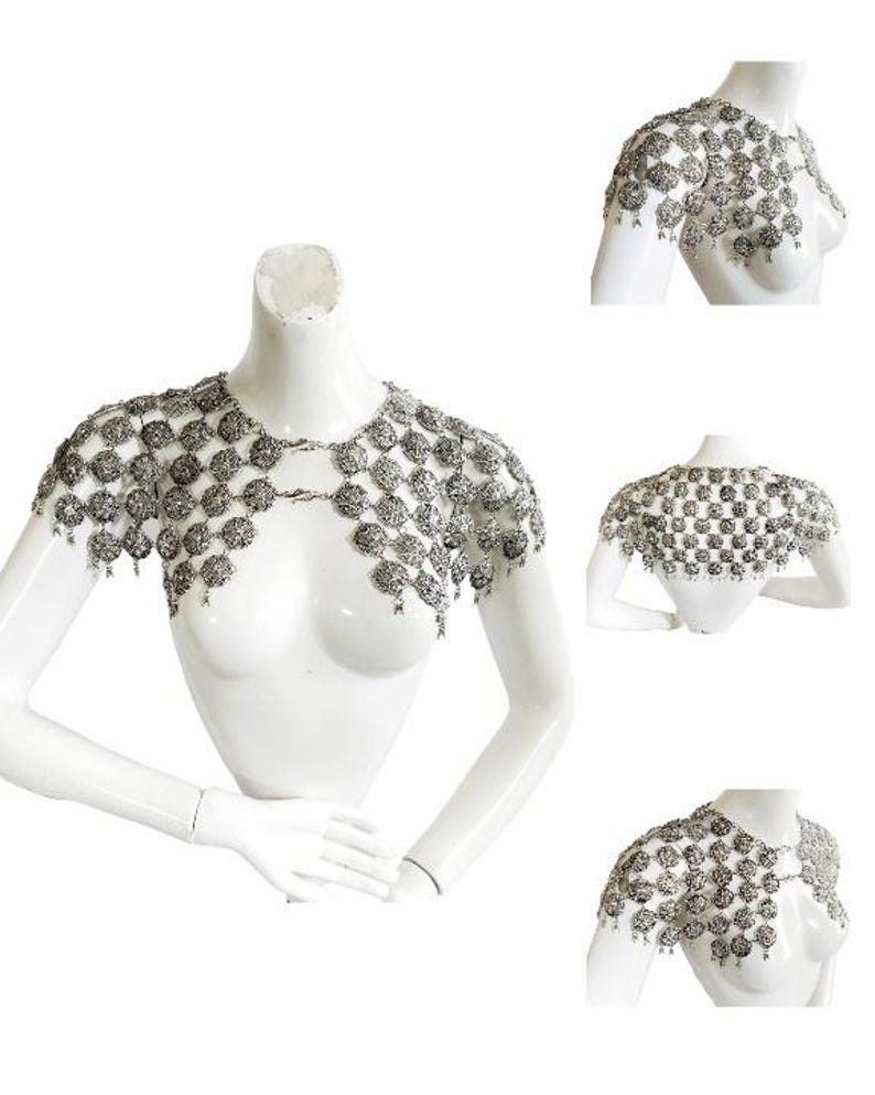 May include: Silver chainmail shoulder piece with a decorative design. The chainmail is made of small, round links that are connected together to form a mesh-like fabric. The shoulder piece is designed to be worn over the shoulders and chest, and it has a flowing, draping effect.