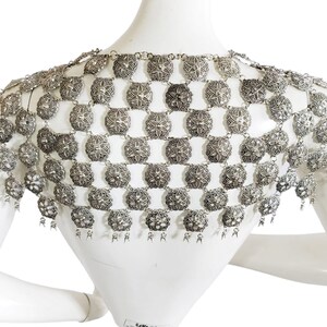 May include: Silver chainmail shoulder piece with a decorative design. The chainmail is made of small, round links that are connected to form a mesh-like fabric. The shoulder piece has a fringe at the bottom.