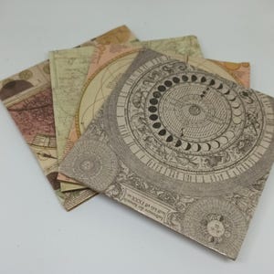 May include: A stack of four square paper napkins with vintage map and celestial designs. The napkins feature a variety of colors, including beige, brown, and pink. The designs include maps, celestial charts, and astronomical illustrations.