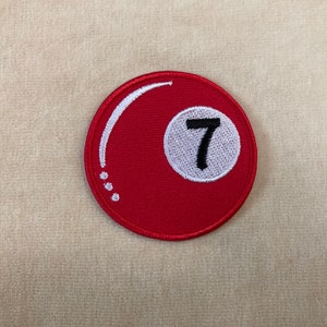 May include: A round, red patch featuring the number 7 inside a white circle. The patch has a white curved design and white dots. This patch is likely for a pool or billiards theme.