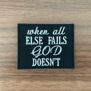 May include: A rectangular black embroidered patch featuring white stitched text that reads when all ELSE FAILS GOD DOESN'T. The patch has a clean, finished border and is designed for application onto fabric surfaces as a decorative accessory.
