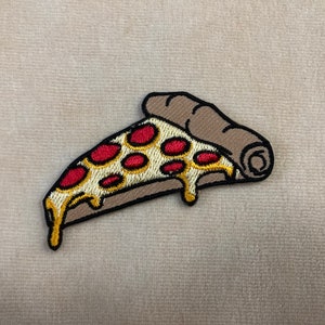 May include: Embroidered pizza slice patch with a brown crust, yellow cheese dripping, and red pepperoni. The patch has a black border and is likely for clothing or accessories.