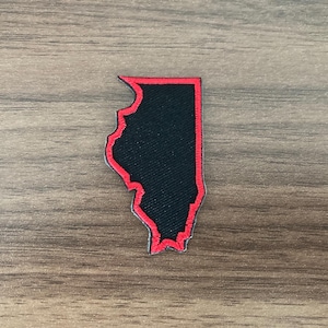 May include: A fabric patch shaped like the state of Illinois, featuring a solid black center with a vibrant red embroidered border outlining the entire perimeter of the state's geographic shape, showcasing a clean and precise stitched edge.