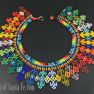 May include: A circular beaded collar necklace featuring a vibrant spectrum of colors including red, orange, yellow, green, blue, and black. The design consists of intricate geometric patterns and fringe-like elements. Text reads East of Santa Fe.com.