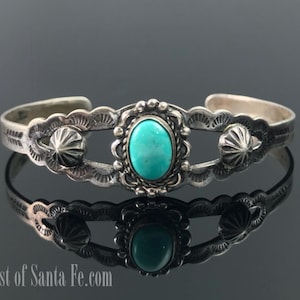 May include: A silver cuff bracelet with an oval turquoise stone in the center, framed by a decorative border. The bracelet features intricate detailing and two decorative silver accents on either side of the turquoise stone.