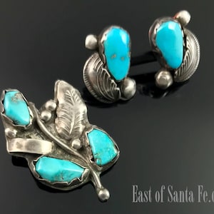 May include: A set of turquoise and sterling silver earrings and a brooch. The earrings are simple, with a single turquoise stone set in a silver setting. The brooch is more elaborate, with a cluster of turquoise stones set in a silver leaf design.