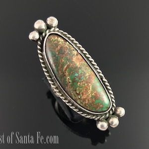 Puede incluir: Un anillo de plata con una piedra ovalada de turquesa verde y marrón engastada en un diseño de cuerda. El anillo tiene tres bolas de plata a cada lado de la piedra.