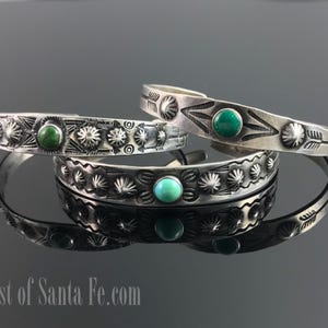 Puede incluir: Tres pulseras de plata con detalles de piedras turquesas y verdes. Las pulseras tienen diseños estampados de rayos de sol y patrones geométricos. Las pulseras se exhiben sobre una superficie reflectante.
