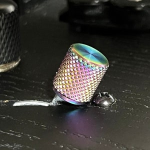 Puede incluir: Primer plano de una perilla iridiscente con patrón de diamante para una guitarra. La perilla es de metal y tiene un tornillo en la parte inferior.